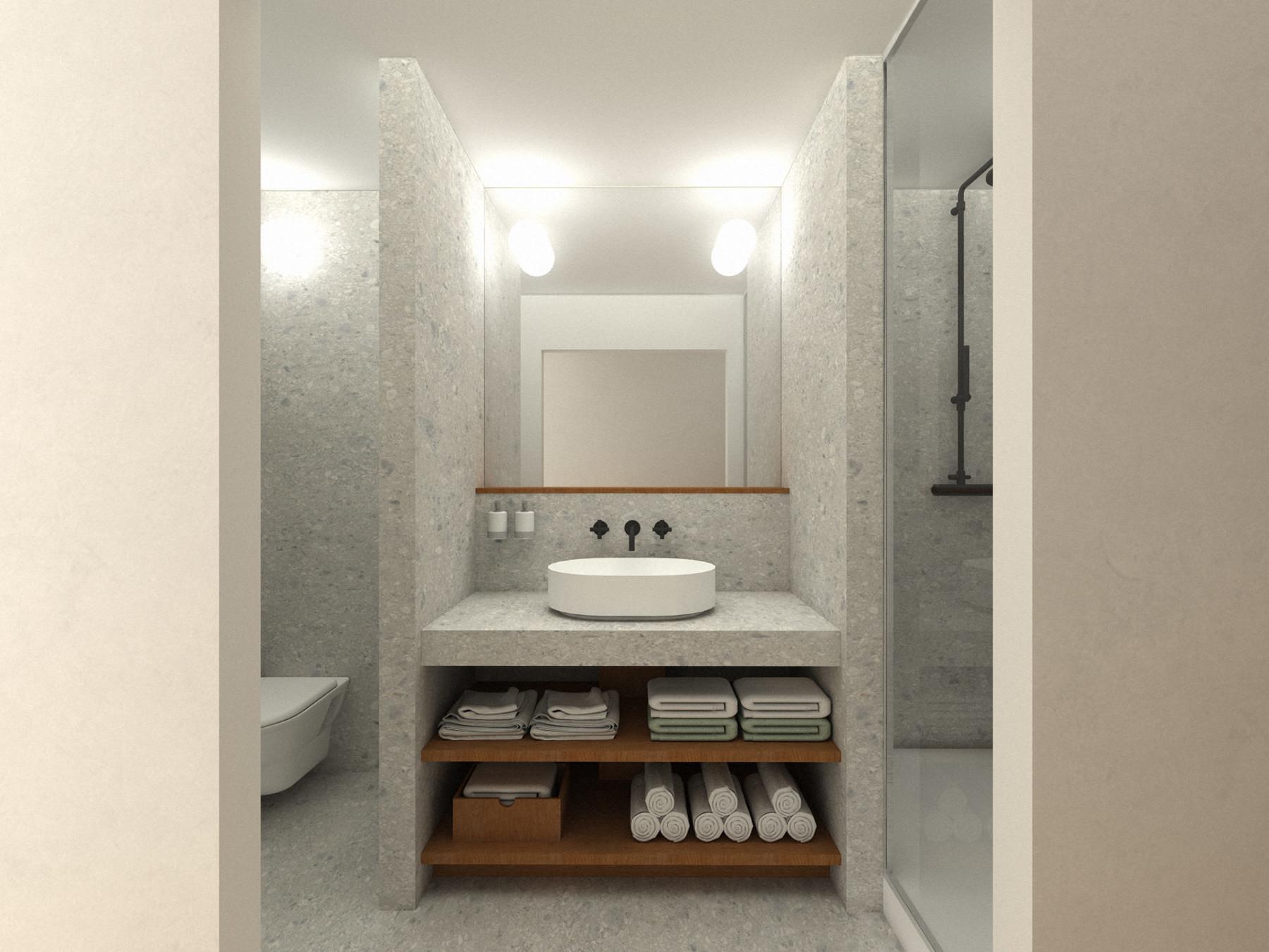 La photo montre une salle de bain contemporaine au design minimaliste et fonctionnel. Le sol et les murs sont recouverts d’un carrelage gris clair effet pierre. Au centre, un meuble vasque en béton clair avec une vasque ronde blanche repose sur un plan de travail assorti. Deux robinets noirs mats (eau chaude et froide) sont encastrés dans le mur au-dessus de la vasque. Deux distributeurs muraux blancs sont fixés à gauche du miroir. Sous le plan de travail, deux étagères en bois contiennent des serviettes soigneusement pliées, des rouleaux de serviettes blanches, et un coffre de rangement. Un grand miroir occupe toute la largeur du mur au-dessus du meuble. À droite, une douche avec paroi vitrée et robinetterie noire. À gauche, une cuvette de toilettes suspendue est partiellement visible derrière une cloison.