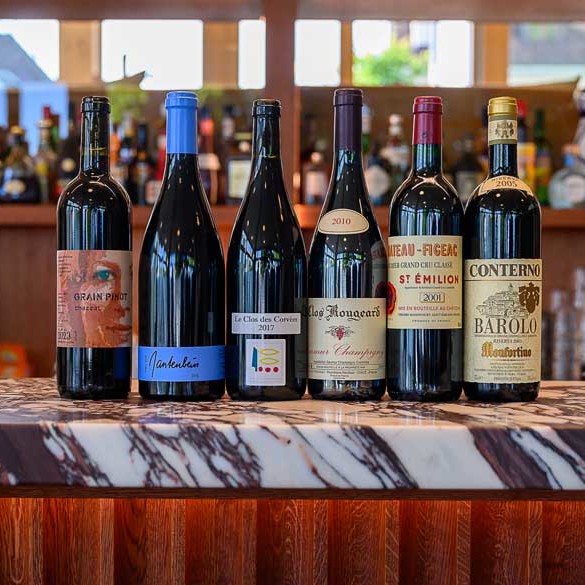 Six bouteilles de vin rouge sur le comptoir du bar du boutique hôtel Port Gitanan à Bellevue Genève. Conseils sur comment choisir un vin rouge pour dîner à l'hôtel