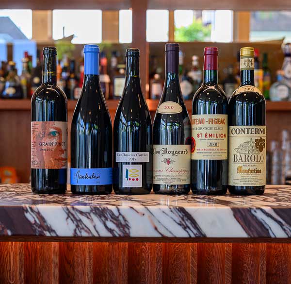 Six bouteilles de vin rouge sur le comptoir du bar du boutique hôtel Port Gitanan à Bellevue Genève. Conseils sur comment choisir un vin rouge pour dîner à l'hôtel